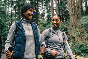 Two ladies hiking through forest wearing Noz reef safe colorful sunscreen on nose